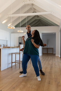 African American couple dancing together in open-plan kitchen near wooden island and pendant lights