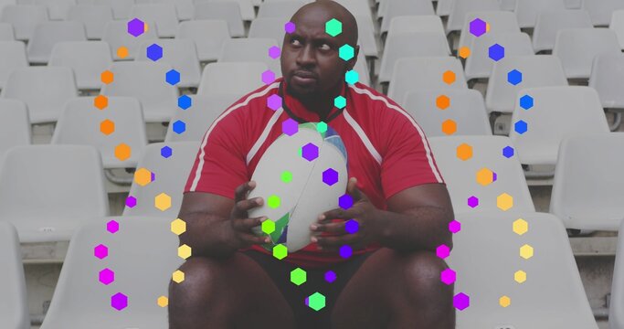 Sitting athlete wearing red jersey holding white rugby ball among stadium white seats with hexagons