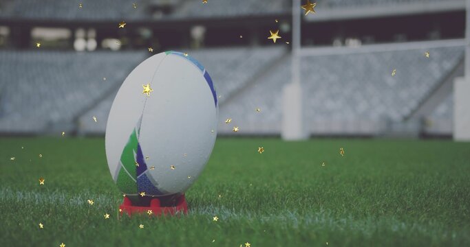 Displaying rugby ball with white green blue panels standing on red tee on stadium grass, confetti