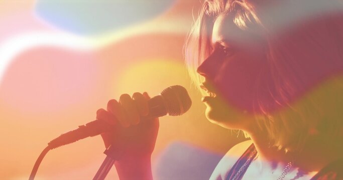 Singing teen singer in sleeveless top, holding wired mic on stage with lens flares, copy space