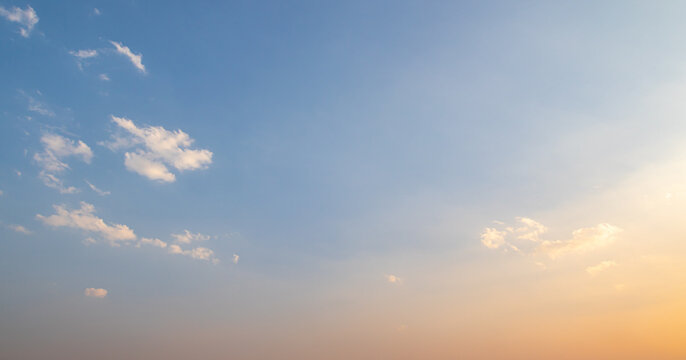 Clear sunset sky with soft orange gradient and small white clouds at twilight for natural background and spiritual concept design