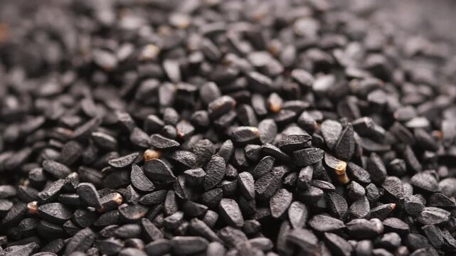Black cumin seeds rotating on surface with extreme macro detail in slow motion video clip.