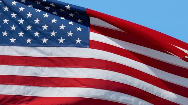 Close-up view of the United States flag with its red and white stripes and blue field of stars waving proudly against a clear blue sky.