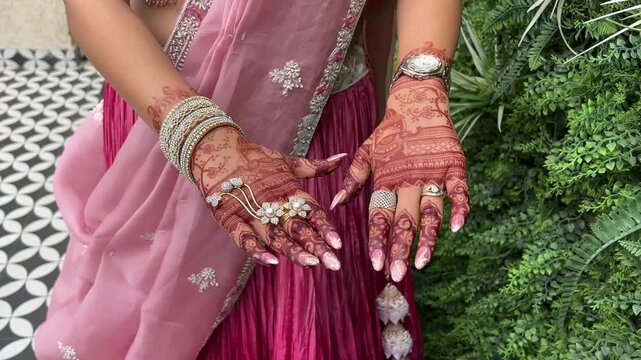 A stunning lifestyle portrait of a bride adorned in a vibrant pink silk lehenga, highlighting the delicate craftsmanship of her designer henna body art.