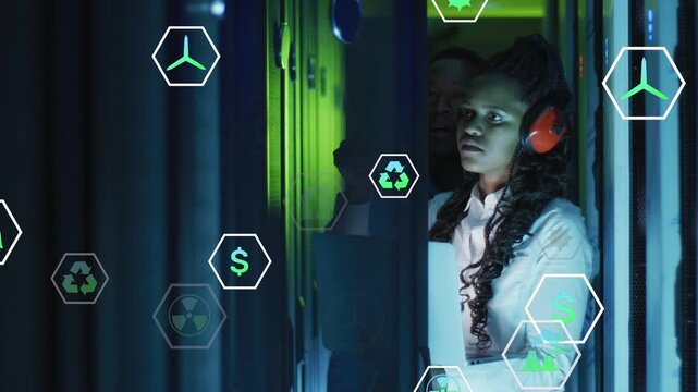 Woman tech using tablet checking racks wearing red muffs while AR hex icons overlaying energy data