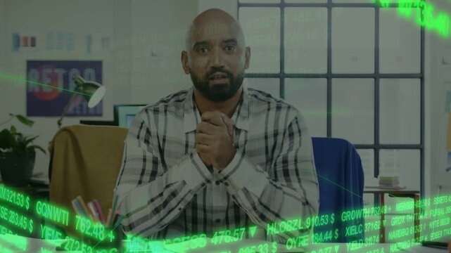 Seated man clasping then opening palms after green ticker overlay, presenting finance to camera