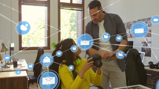 Seated woman using DSLR while editor tapping tablet, envelope icon sparking overlay across prints