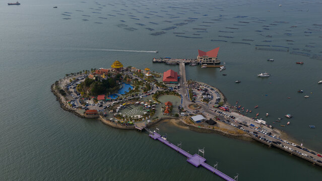 Aerial view of Ko Loi island featuring the golden-roofed temple, parking areas, and a purple pier surrounded by fish farms in the sea in Chon Buri, Thailand.