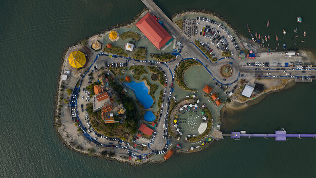 Aerial view of Ko Loi island park with its temple buildings, blue pond, and busy parking lots surrounded by the sea in Chon Buri, Thailand.