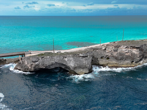Aerial view of the Glass Window Bridge on a narrow rocky strip separating the turquoise Caribbean Sea and deep blue Atlantic Ocean with a car in North Eleuthera, North Eleuthera, The Bahamas.