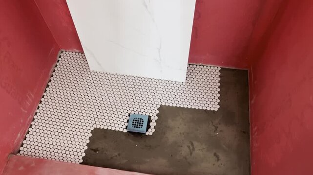 Bathroom floor in progress during renovation, with mosaic tile and drain, unfinished interior.
