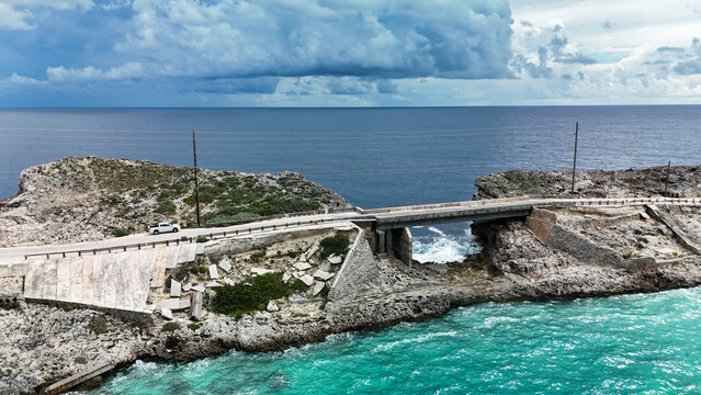 Aerial view of the Glass Window Bridge spanning rocky cliffs between the dark Atlantic Ocean and turquoise Bight of Eleuthera in North Eleuthera, North Eleuthera, The Bahamas.