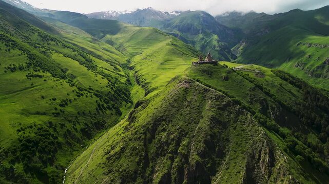 Epic mystery fantasy mountain church aerial panorama. 
Cinematic drone forward flight over lush green valley 
hill towards ancient historic monastery under storm clouds.
