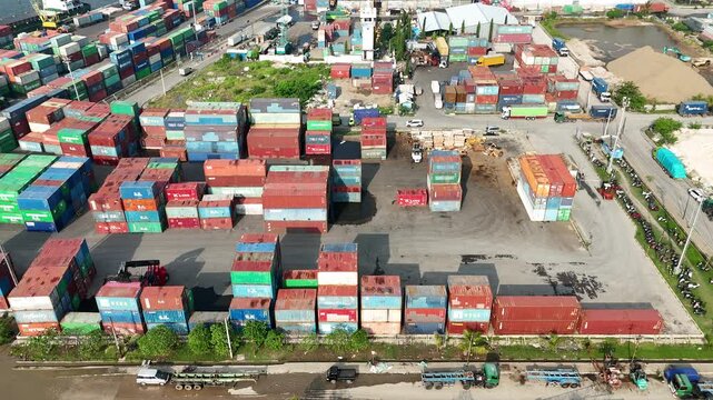 High angle aerial view of a reach stacker crane lifting a pink shipping container onto a heavy-duty truck trailer amidst rows of colorful stacked cargo containers at a busy industrial port.