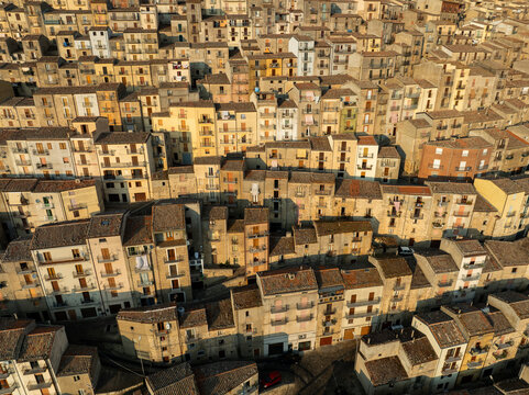Aerial view of the historic stone houses and terracotta rooftops of the medieval village under warm sunlight in Gangi, Sicily, Italy.