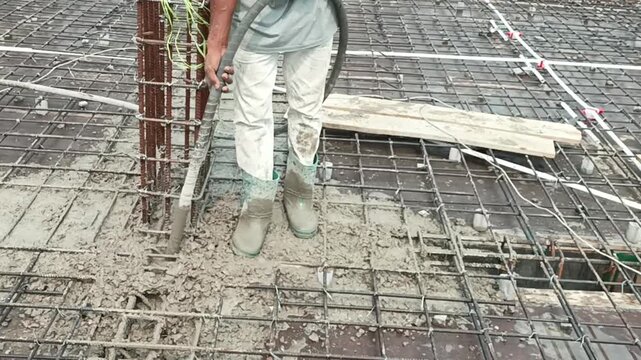 Construction worker using a concrete vibrator on a reinforced steel rebar mesh building floor