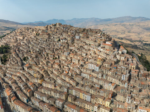 Aerial view of the historic hilltop town of Gangi with its densely packed stone houses and terracotta roofs against a backdrop of rolling hills in Gangi, Sicily, Italy.