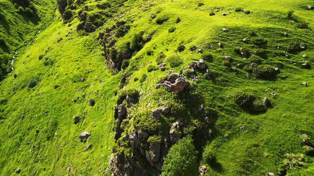 Cinematic 4K ProRes 422 aerial orbit and descent reveal of a mountain stream in a green ravine. Man standing on ancient ruins, Georgia.