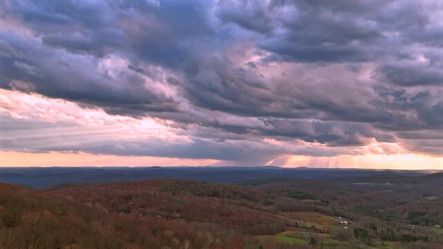 A breathtaking aerial hyperlapse looking out over a vast forested mountain valley at sunset. Mountains recede into haze on the horizon. Shot from an elevated position in the Catskill Mountains region 