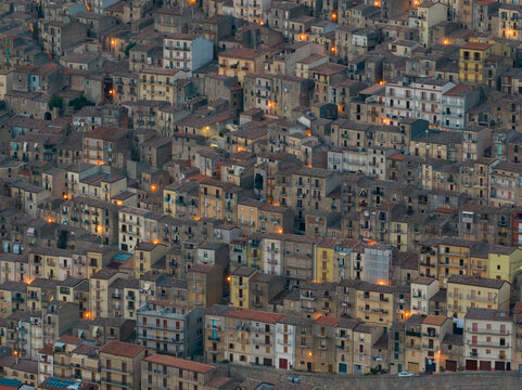 Aerial view of the historic hillside town featuring dense stone houses and terracotta rooftops during twilight in Gangi, Sicily, Italy.