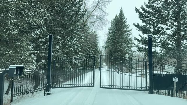 The homeowner is opening an automatic gate to enter their snow-covered house, which winds through the woods, revealing a frigid winter landscape covered in frost and ice in the quiet stillness of Dece