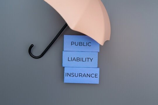 Umbrella covers stacked blue blocks with text PUBLIC LIABILITY INSURANCE. Protection and insurance concept.