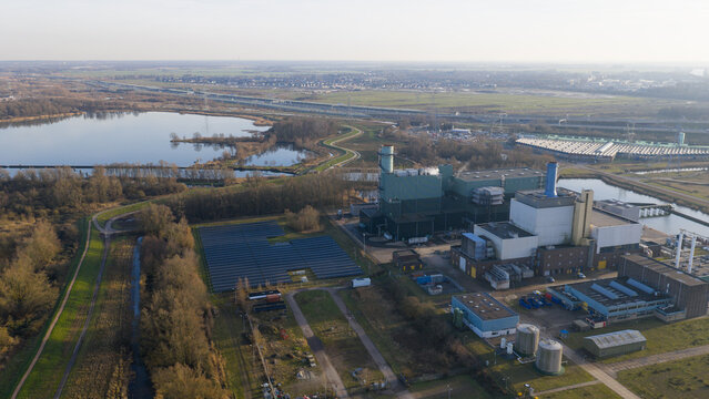 Aerial view of the Vattenfall Elektriciteitscentrale Diemen power plant featuring industrial buildings, solar panel arrays, and a nearby lake under a clear sky in Diemen, Noord-Holland, Netherlands.