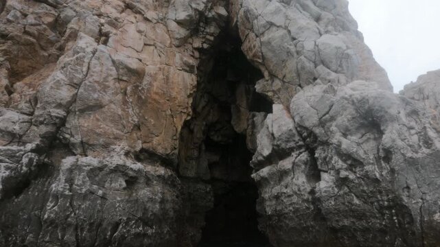 Rugged limestone cave opening carved into coastal cliffs at Souda Bay, Chania, Greece. Misty overcast sky frames jagged rock formations at a premier freediving location.