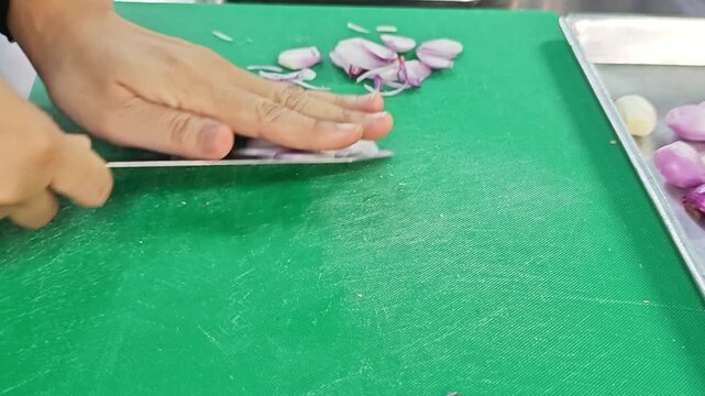 Close up of chef's hands slicing fresh shallots with a sharp knife on a green cutting board.
