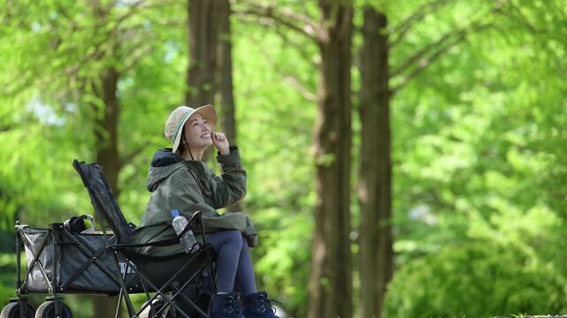 新緑の森の中でキャンプチェアに座るでくつろぐ笑顔の女性の横顔、ソロキャンプアウトドア　景色を眺める動画