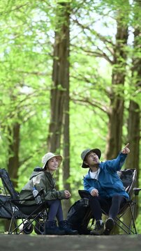 新緑のキャンプ場で椅子に座る笑顔のアウトドアやレジャーを楽しいミドルの夫婦　鳥や景色を眺める縦動画　指を差して見つめる