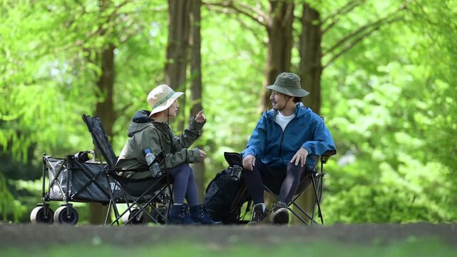 新緑のキャンプ場で椅子に座る笑顔のアウトドアやレジャーを楽しいミドルの夫婦　楽しく会話をするシーンの動画