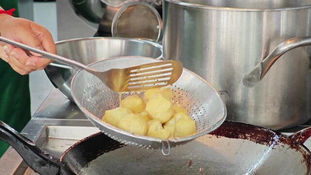 Chef using a stainless steel strainer to scoop up crispy fried tofu from a wok, oil draining process.