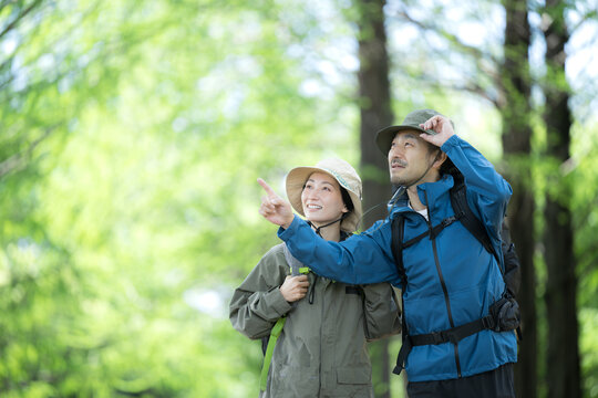 新緑のトレッキングや登山で笑顔のアウトドアやレジャーを楽しいミドルの夫婦　鳥や景色を眺める指を差す