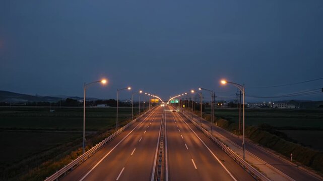 Highway outskirts with sparse traffic and glowing amber streetlights just before the break of dawn