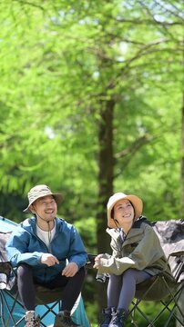 新緑のキャンプ場で椅子に座る笑顔のアウトドアやレジャーを楽しいミドルの夫婦　鳥や景色を眺める縦動画