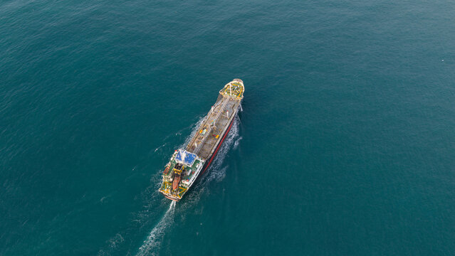 Aerial view of a large industrial tanker ship navigating through deep blue ocean waters with a white wake off the coast of Tambon Map Ta Phut, Chang Wat Rayong, Thailand.