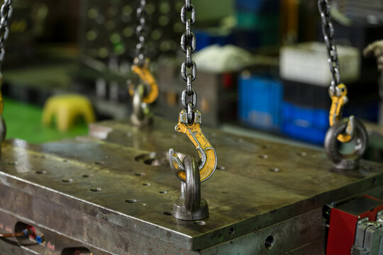 Yellow hoist hook hangs above steel lifting eye on mold surface, ready for controlled lifting, safe die handling, and maintenance workflow during production changeover in factory workshop line