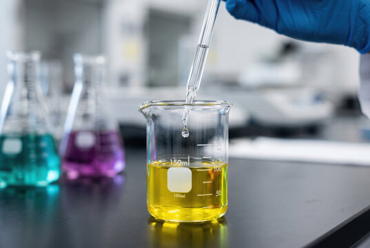 Glass dropper adding clear liquid to a beaker of yellow fluid in a modern chemistry laboratory
