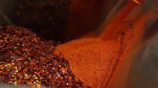 Pouring red pepper powder onto dried chili flakes, creating a mix of spicy culinary ingredients