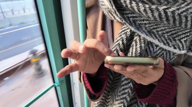 Woman hands using smartphone while commuting on tram during winter day in european city.