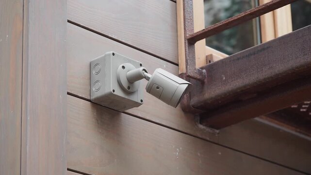 Security camera mounted on a wooden wall next to a metal railing footage.