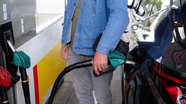 Mid Shot of Unrecognizable Man Hands Pressing Fuel Pump Handle Lever While Refueling Car at Gas Station During Rising Fuel Prices and Cost of Living Increase, Part of a Series.