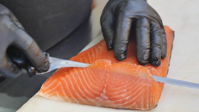 Skilled chef cuts fresh atlantic salmon fillet on white cutting board in professional kitchen.