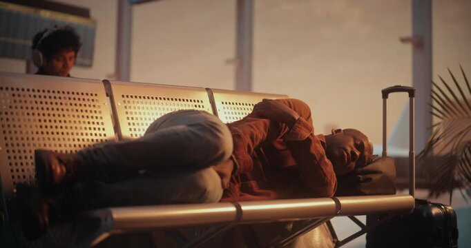 Weary African American Male Passenger in Overshirt Attempts to Get Some Rest While Waiting For Boarding Call. Man Curled Up on Airport Benches. Concept of Struggle to Find Comfort in Public Spaces.