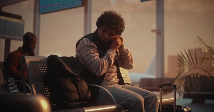 Sitting in Departure Lounge During Warm Sunset, Young Man With Curly Hair Puts Earrings Back On. Having Removed Them Earlier Pass Via Metal Detector and Security Screening, Now Prepares For Flight.