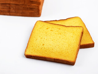 Fototapeta premium Close-up of sliced pumpkin bread with a vibrant golden-orange color placed on a white background, with a loaf in the background. The image highlights the soft, airy crumb and lightly crisp edges.