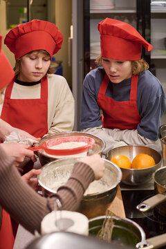 Vertical shot of Caucasian teenagers learning baking, watching dough preparation in cooking class. Supporting culinary education, youth skills training, school program marketing