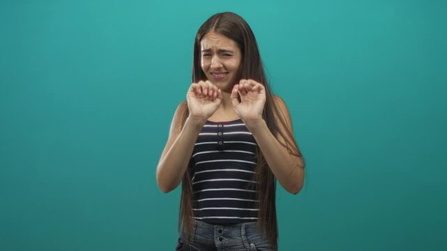 Teenage girl wearing braces and striped tank top holds hands up with palms out in studio while stepping back and wincing; fear.