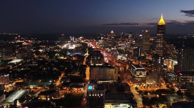 Cinematic nighttime aerial footage of the illuminated Atlanta skyline, featuring the iconic cylindrical Westin Peachtree Plaza tower and city lights.